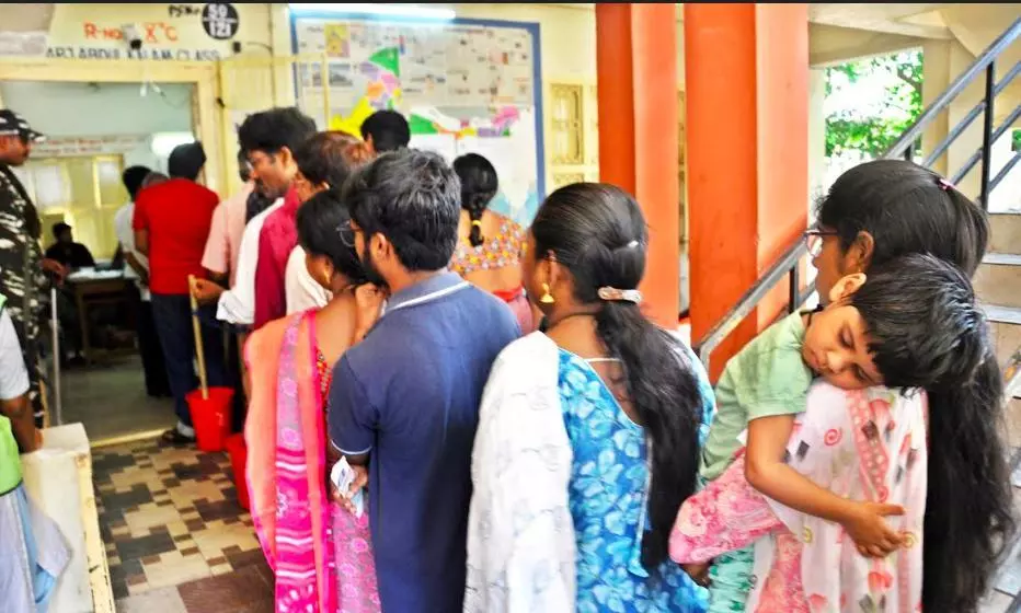 A mother waits in a queue with her kid to cast their vote at Nagaraju Municipal school in Rajamahendravaram on Monday.  - A.MANIKANTA KUMAR